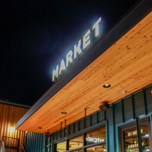 A close-up of a building's exterior featuring a sign that reads "MARKET" above a glass entrance.
