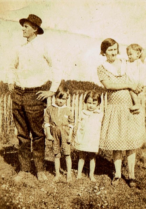 A vintage photo of a man, woman, and three children standing outdoors near a wooden fence.