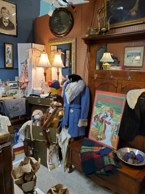 A vintage display featuring clothing, lamps, and framed art in a cozy, eclectic setting.