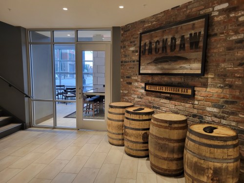 Interior of a coffee and bourbon bar named "Jackdaw," featuring a brick wall and wooden barrels.