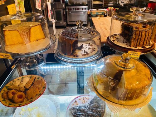 A display of various cakes under glass domes, including a honey cake, chocolate cake, and a layered dessert.