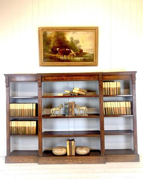 A wooden bookshelf with books, decorative horse figurines, and a painting of cows above it.
