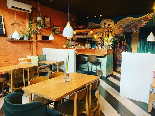 Cozy café interior with wooden tables, green accents, and a vibrant bar area featuring plants and colorful decor.