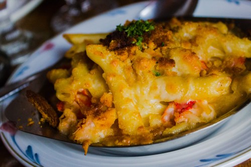 A close-up of baked macaroni and cheese topped with breadcrumbs and herbs, served in a silver dish.