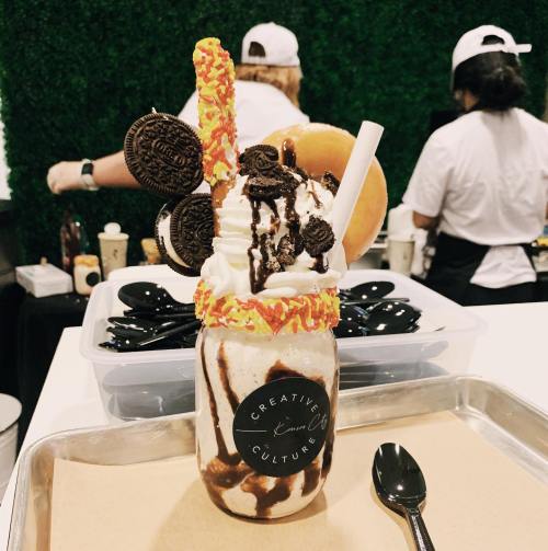 A colorful milkshake topped with whipped cream, Oreos, a donut, and a candy stick, served in a jar.