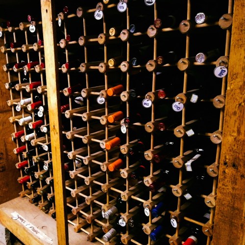 A wooden wine rack filled with various bottles, each labeled and organized in rows.