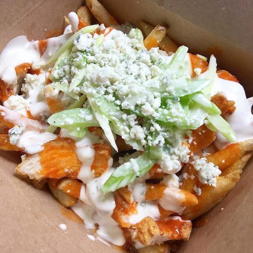 A box of loaded fries topped with buffalo sauce, blue cheese, and green onions.