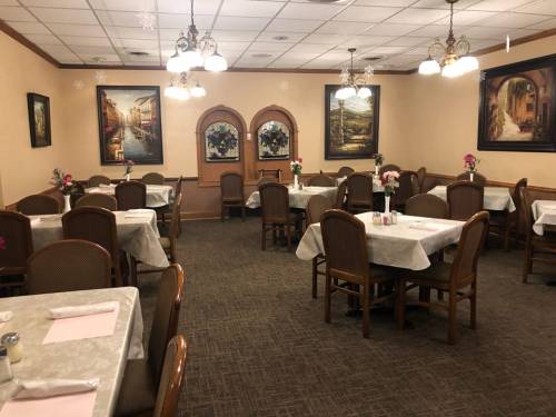 A cozy restaurant interior with tables set for dining, featuring floral centerpieces and decorative paintings on the walls.