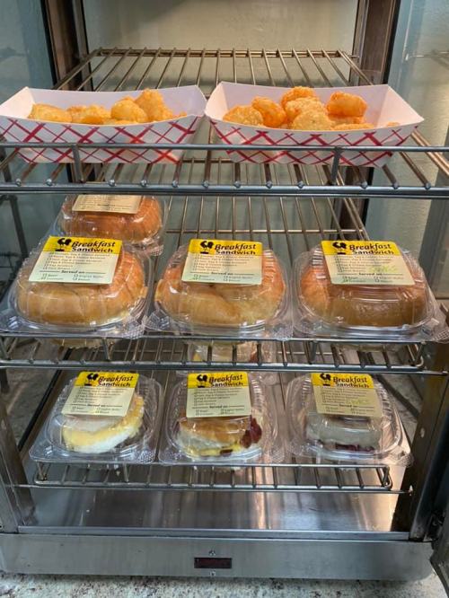 A display case with various breakfast items, including pastries and tater tots, neatly arranged in plastic containers.
