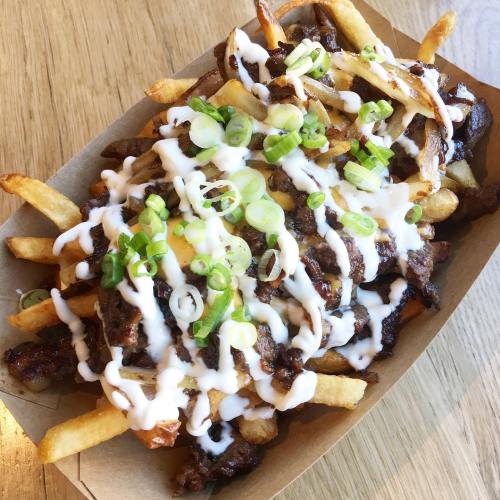 A tray of loaded fries topped with grilled meat, green onions, and drizzled with white sauce.