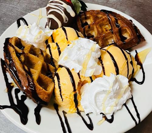 A plate with two waffles, three scoops of ice cream, whipped cream, and a chocolate-covered strawberry.