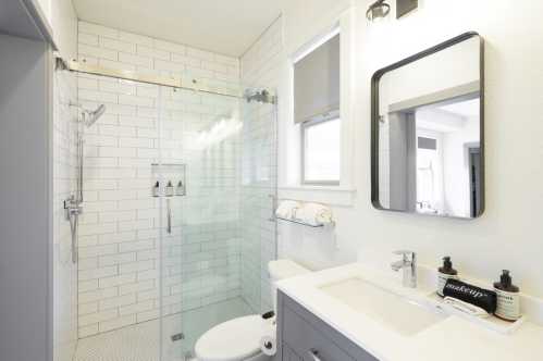 Modern bathroom featuring a glass shower, white tiles, a sleek vanity, and neatly arranged toiletries.