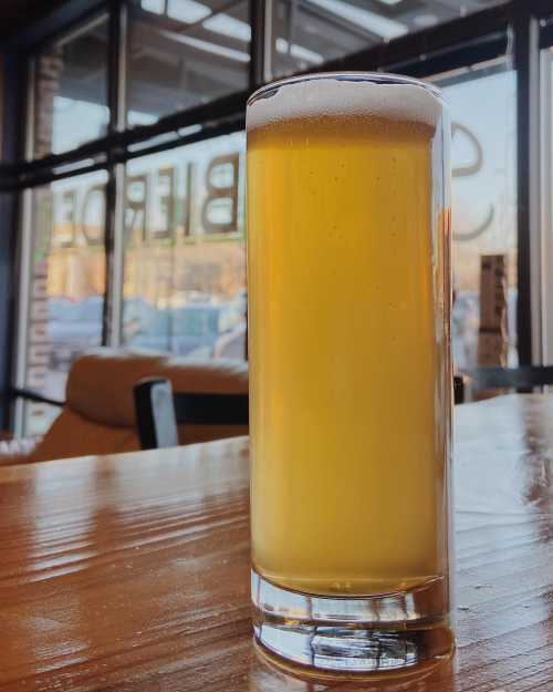 A tall glass of golden beer with a frothy head, sitting on a wooden table in a cozy bar setting.