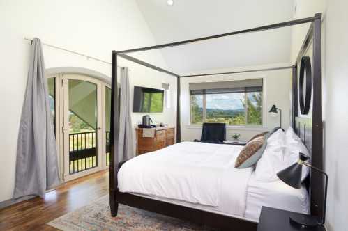 Bright bedroom with a four-poster bed, large windows, and a view of nature. Modern decor and cozy atmosphere.