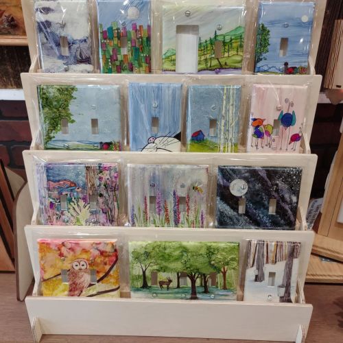 A display of colorful art pieces featuring landscapes, animals, and abstract designs on light switch covers.