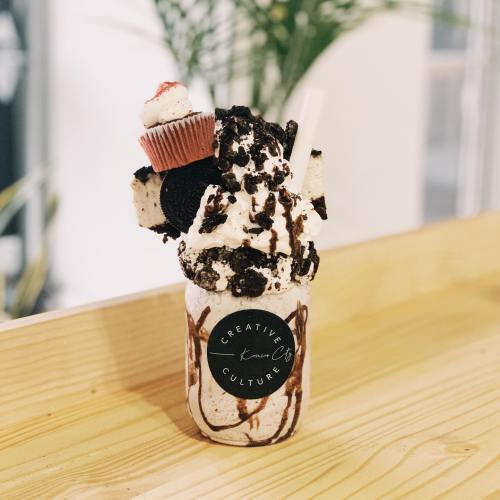 A decadent milkshake topped with whipped cream, chocolate drizzle, cookies, and a mini cupcake in a jar.