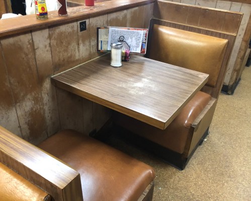 A small wooden table with two brown leather booths in a diner setting, featuring a salt shaker and a menu.