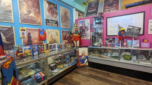 A colorful display of Supergirl memorabilia, including posters, toys, and costumes in a vibrant room.