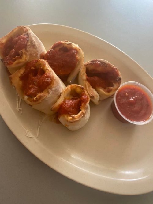 A plate of five stuffed bread rolls topped with marinara sauce, accompanied by a small cup of extra sauce.
