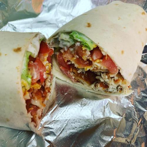 A close-up of a cut burrito filled with chicken, lettuce, tomatoes, and sauce, wrapped in foil.