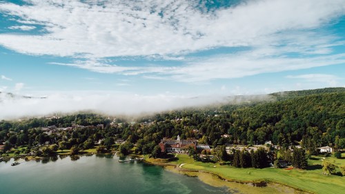 Aerial view of a lush green landscape with a lake, clouds, and a charming town nestled among the trees.