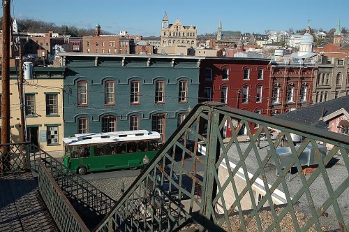 A view of colorful historic buildings and a green trolley bus in a quaint town, with a clear blue sky above.