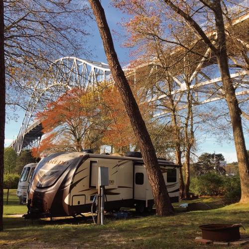 An RV parked under a bridge, surrounded by autumn trees with colorful leaves.