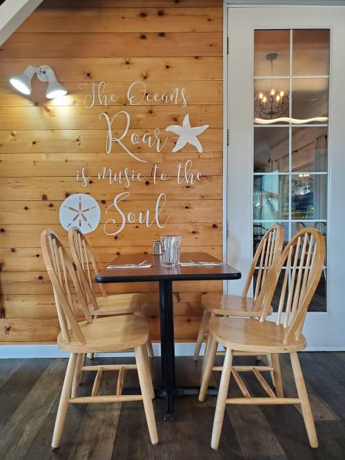 A cozy restaurant setting with a wooden wall, a table for two, and a quote about the ocean's music to the soul.