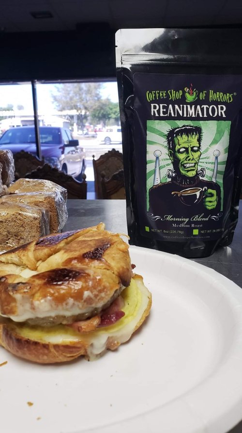 A bag of "Reanimator" coffee next to a plate with a sandwich on a table in a coffee shop.