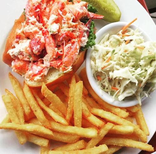 A lobster roll topped with lobster meat, served with coleslaw and a side of golden French fries.