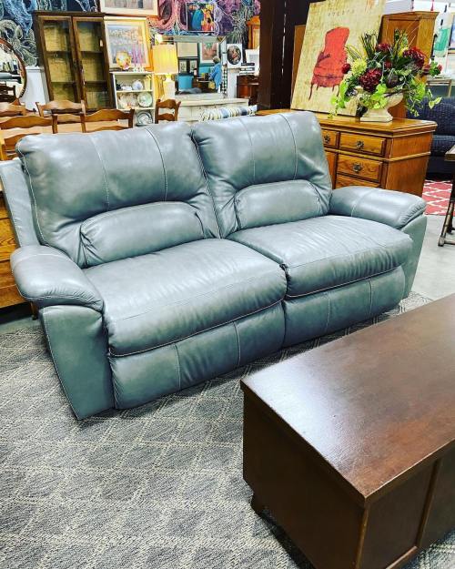 A gray leather sofa with two seats, placed in a furniture store, next to a wooden coffee table.