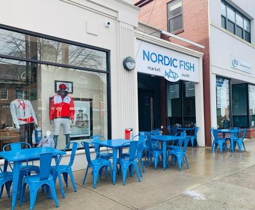 Exterior of Nordic Fish market and sushi restaurant, featuring blue outdoor seating and mannequins in red and white attire.