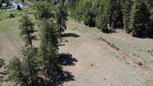Aerial view of a group biking along a dirt path through a forested area near a river.