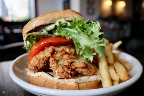 A close-up of a crispy chicken sandwich with lettuce, tomato, and sauce, served with a side of French fries.