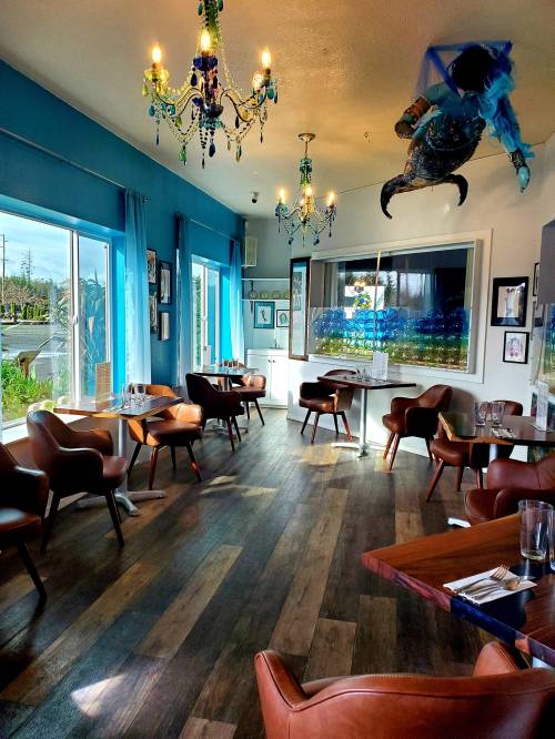A bright restaurant interior with blue walls, wooden floors, and unique decor, including a suspended figure and chandeliers.
