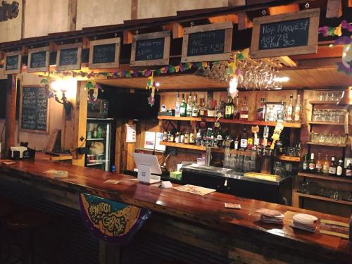 A rustic bar with a wooden counter, shelves of liquor, chalkboard menus, and festive decorations.