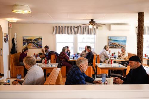 A cozy diner scene with groups of older adults chatting and enjoying meals at wooden booths, surrounded by colorful artwork.