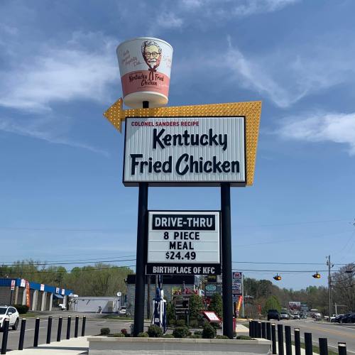 Sign for Kentucky Fried Chicken featuring Colonel Sanders' image, with a drive-thru and meal pricing displayed.