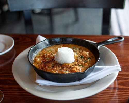 A cast iron skillet with creamy dish topped with rice and herbs, served on a wooden table.