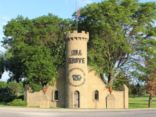 A stone tower with a flag, surrounded by trees, featuring the words "Ida Grove" on its front.