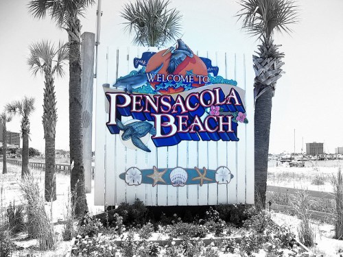 Welcome sign for Pensacola Beach, featuring palm trees and beach-themed decorations.