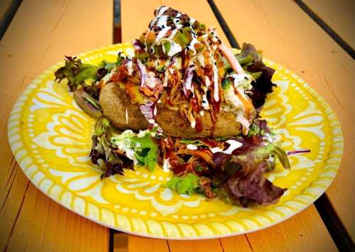 A colorful plate featuring a loaded baked potato topped with coleslaw, drizzled sauces, and served on a bed of greens.