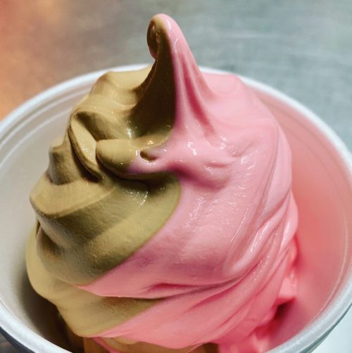 A close-up of a swirl of pink and brown soft serve ice cream in a cup.