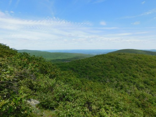 A panoramic view of lush green hills under a blue sky with scattered clouds.