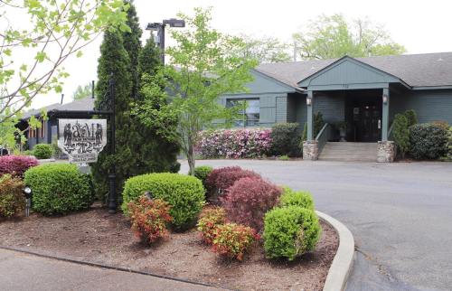 A green building with a sign, surrounded by colorful shrubs and trees, on a paved path.