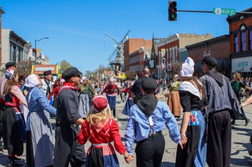 A lively street festival with people in traditional costumes dancing together under a clear blue sky.