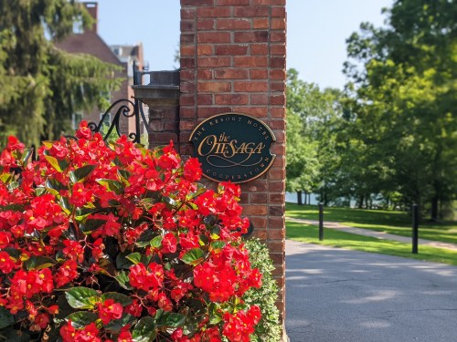 Sign for The Otesaga Resort Hotel surrounded by vibrant red flowers and lush greenery.