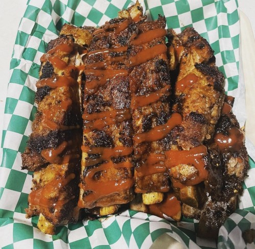 A basket of grilled ribs drizzled with barbecue sauce, resting on green and white checkered paper.