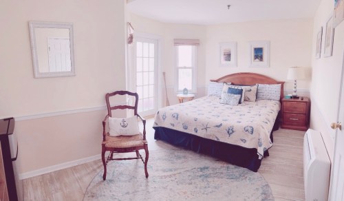 Cozy bedroom with a patterned bedspread, wooden furniture, and natural light from large windows.