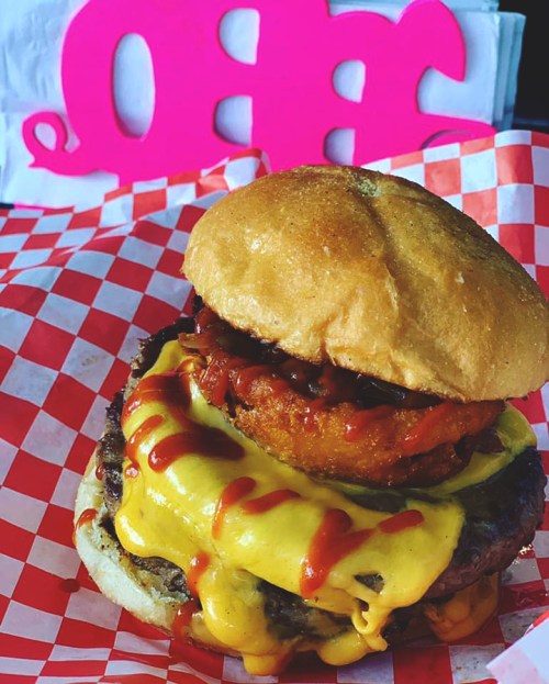 A juicy cheeseburger with melted cheese, crispy onion rings, and ketchup on a toasted bun, served in a checkered wrapper.
